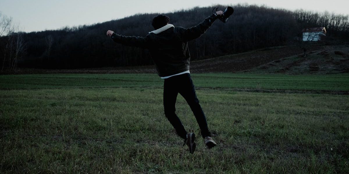 A person joyfully jumps in a serene open field at twilight, capturing a sense of freedom and adventure.