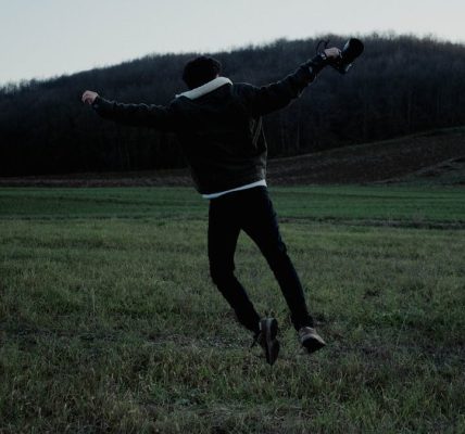 A person joyfully jumps in a serene open field at twilight, capturing a sense of freedom and adventure.