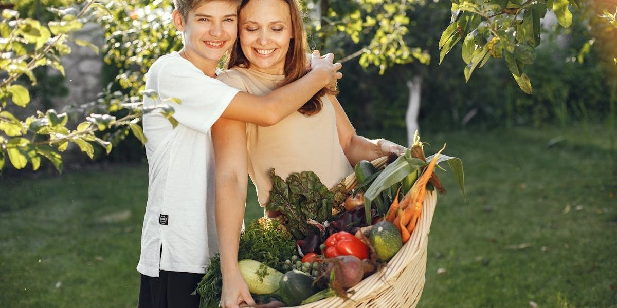 Mother and son smiling outdoors with a basket full of fresh vegetables, embracing in a sunny garden.