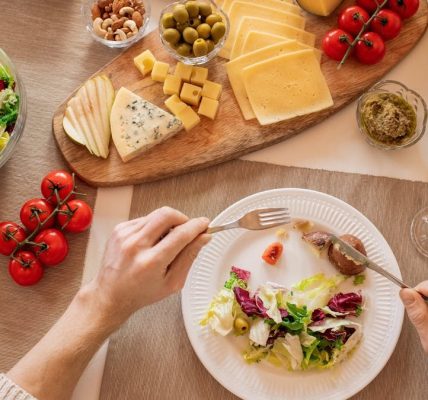Overhead view of a cheese platter with fresh salad and juice, perfect for a gourmet lunch setting.