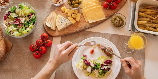 Overhead view of a cheese platter with fresh salad and juice, perfect for a gourmet lunch setting.